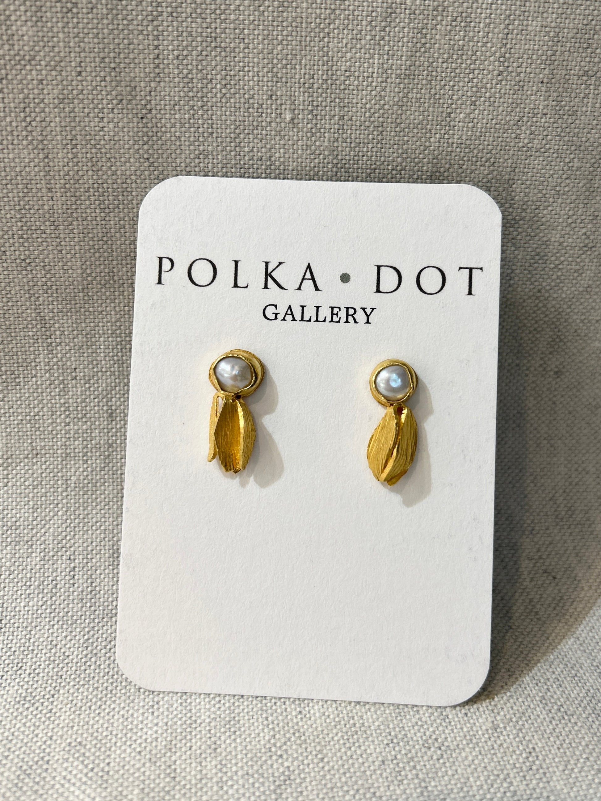 Gold earrings with pearl-like stones on a Polka Dot Gallery card against a textured beige background