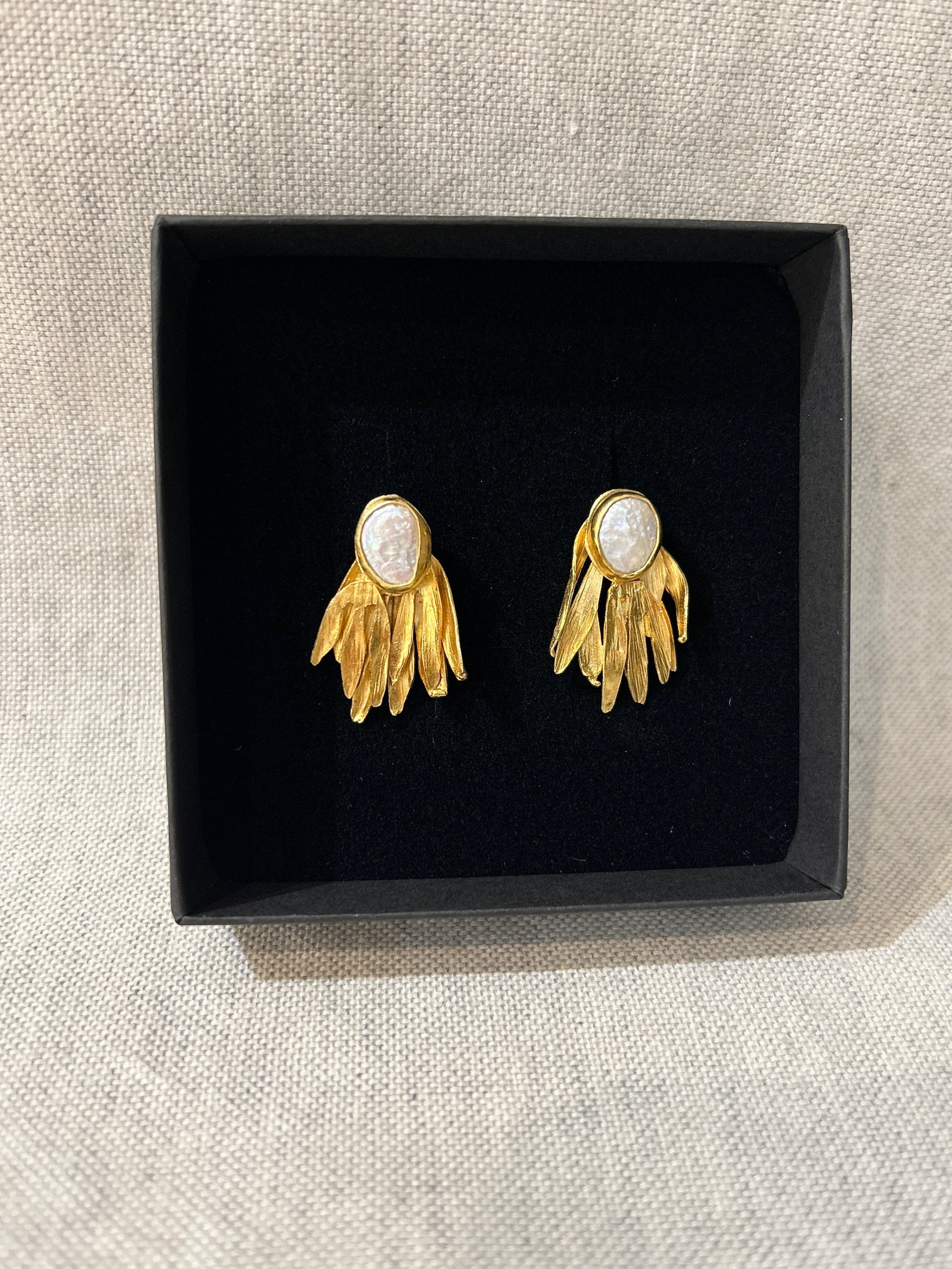 Gold earrings with pearl-like centers in a black box on a beige surface