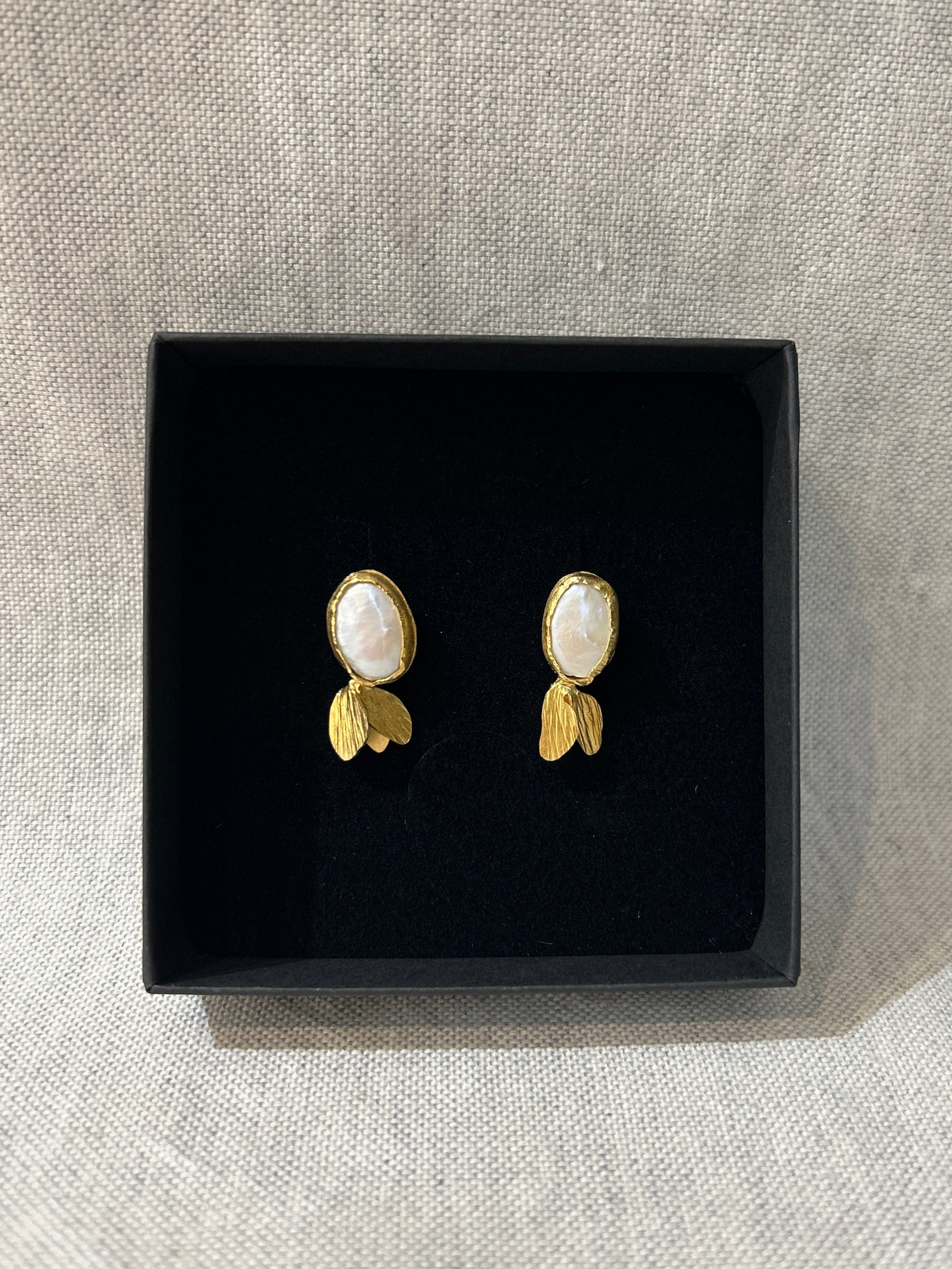 Pair of pearl earrings on a black box with a light gray background