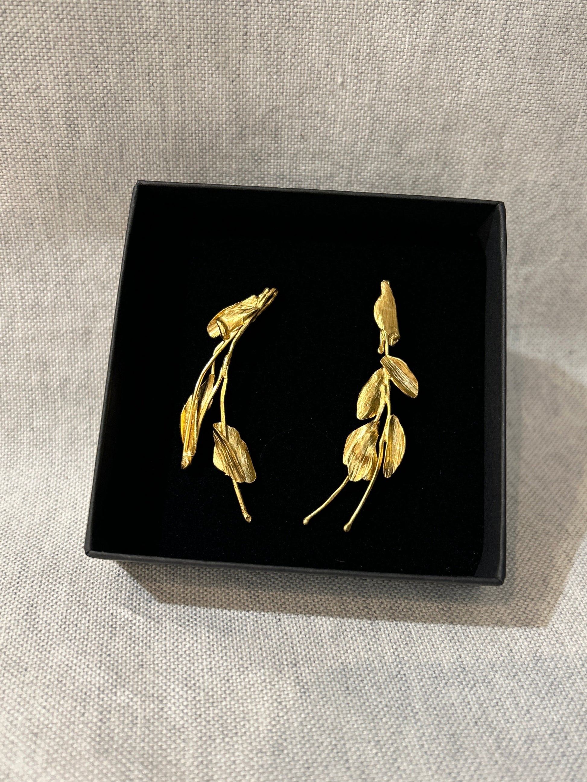 Gold leaf-shaped earrings on a black box with a light gray background