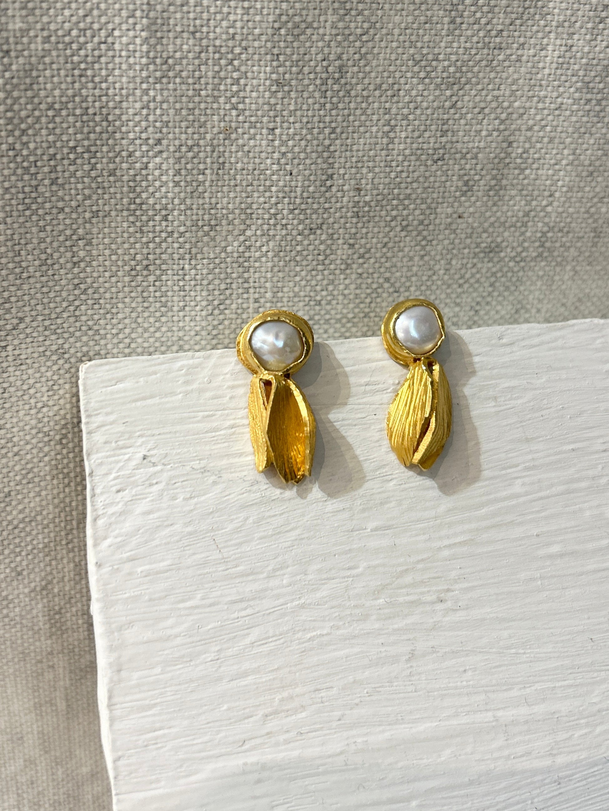 Gold earrings with pearl-like centers on a textured surface