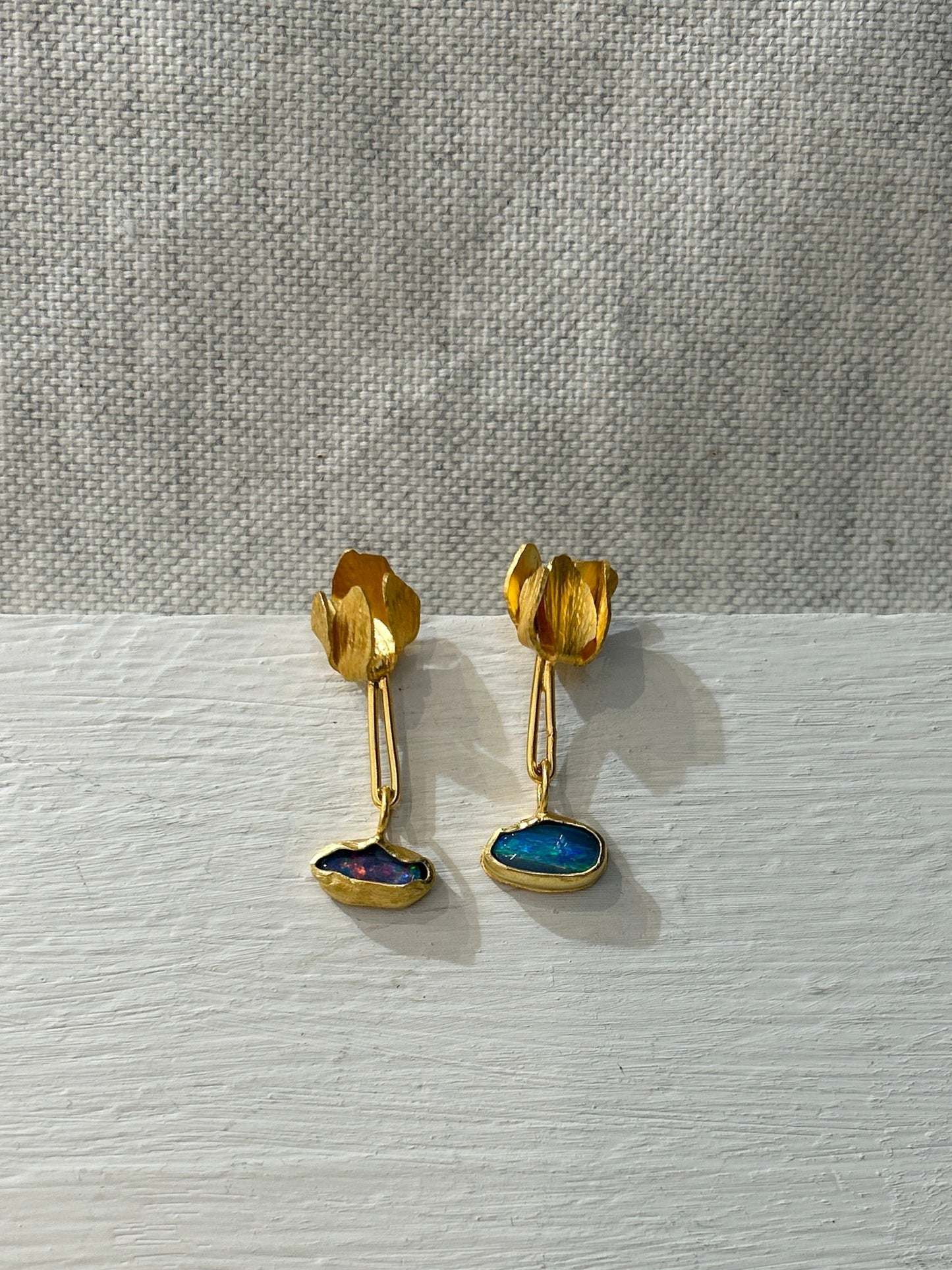 Pair of gold earrings with blue stones on a textured white surface