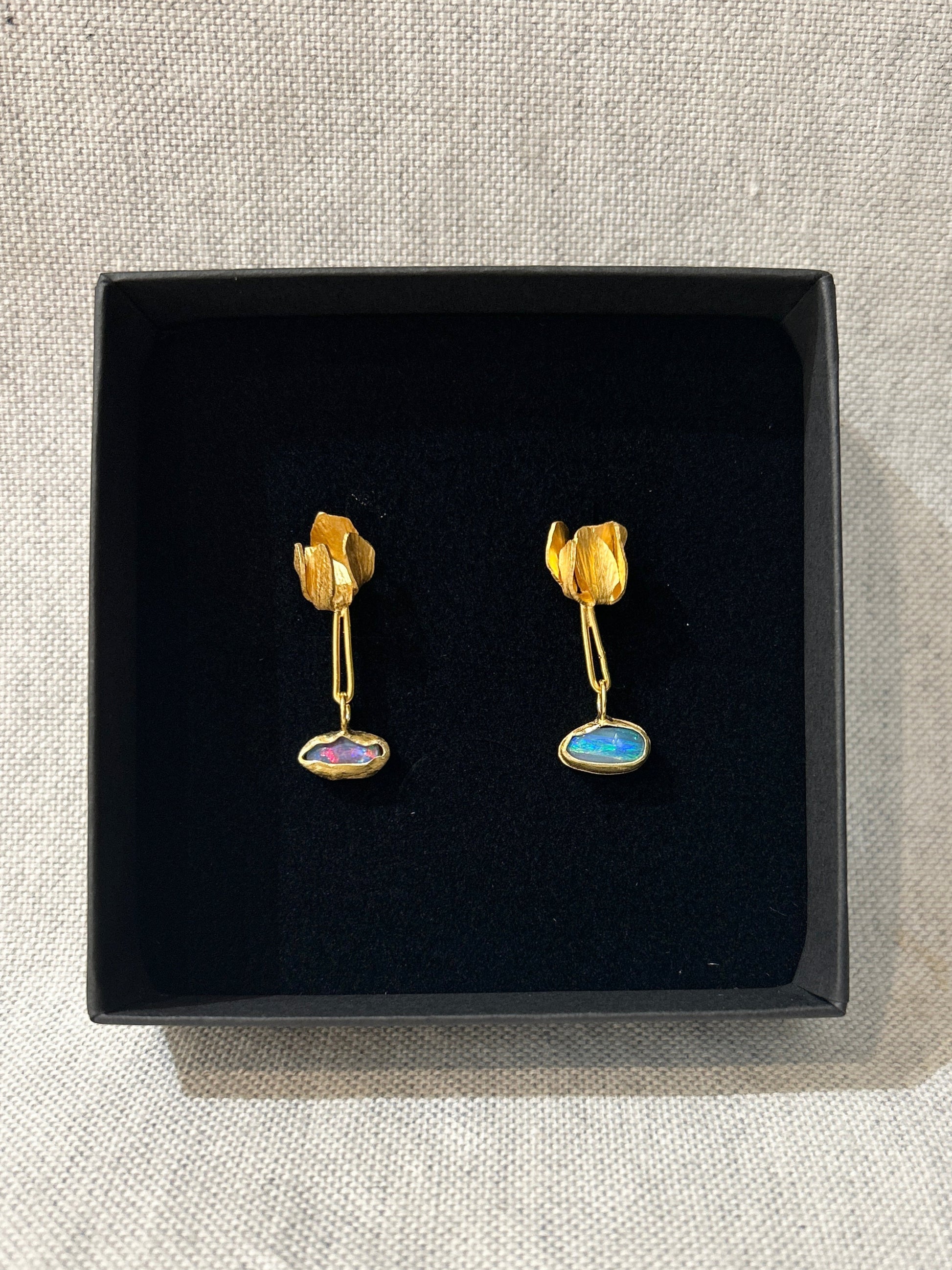 Pair of gold earrings with gemstones in a black box on a textured surface