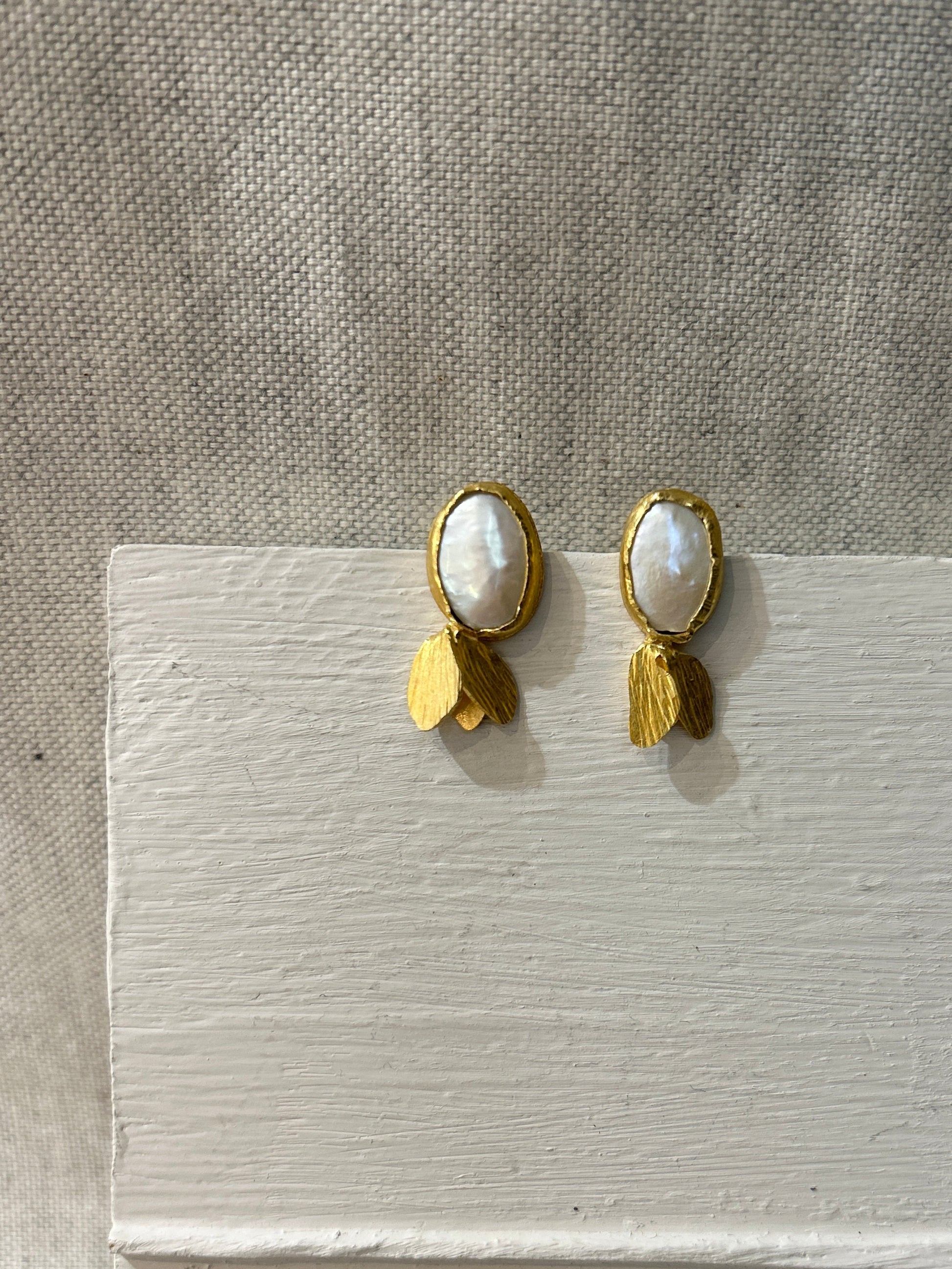 Pair of gold earrings with a pearl on a textured surface