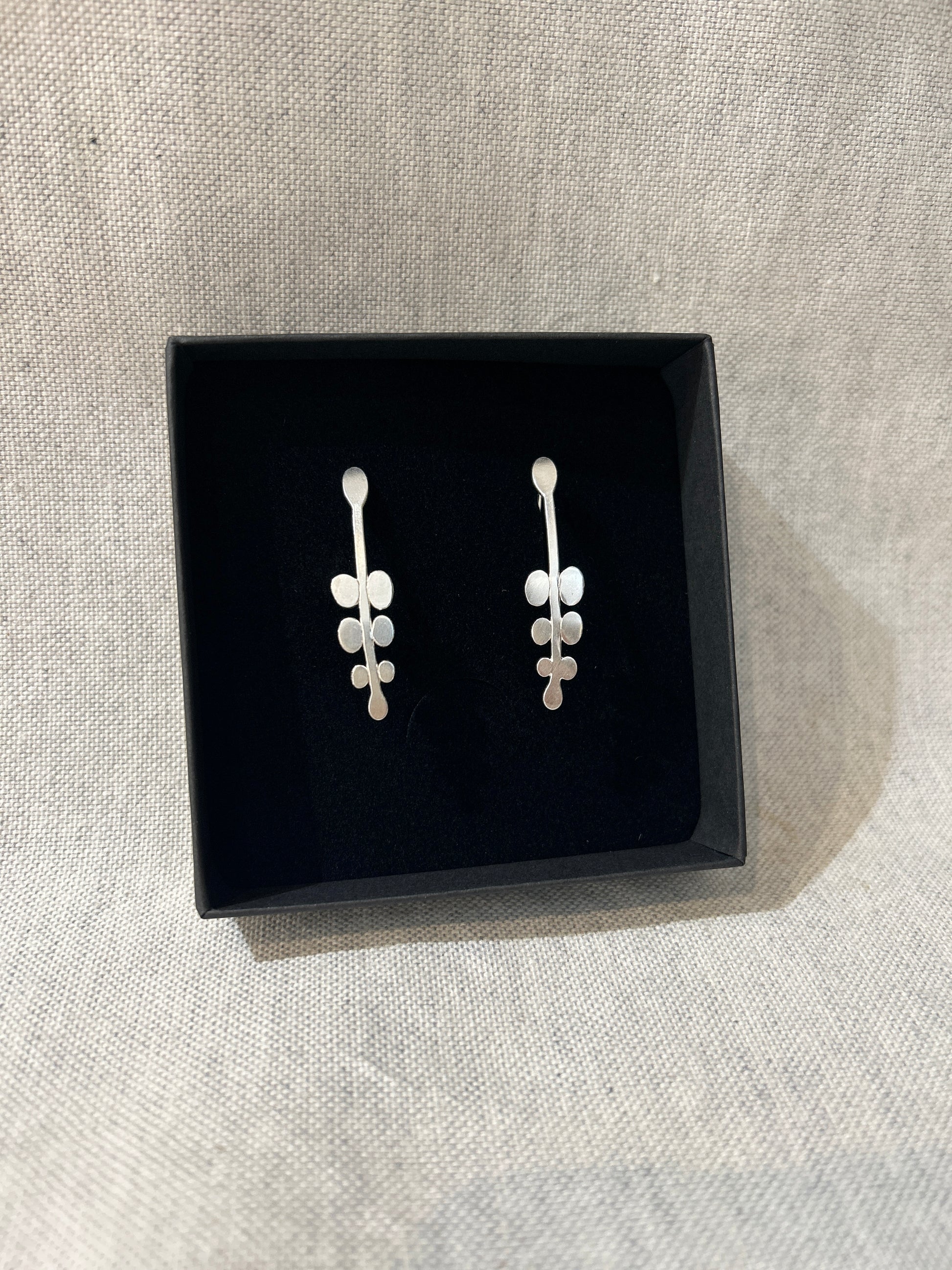 Pair of silver earrings in a black box on a light gray fabric background