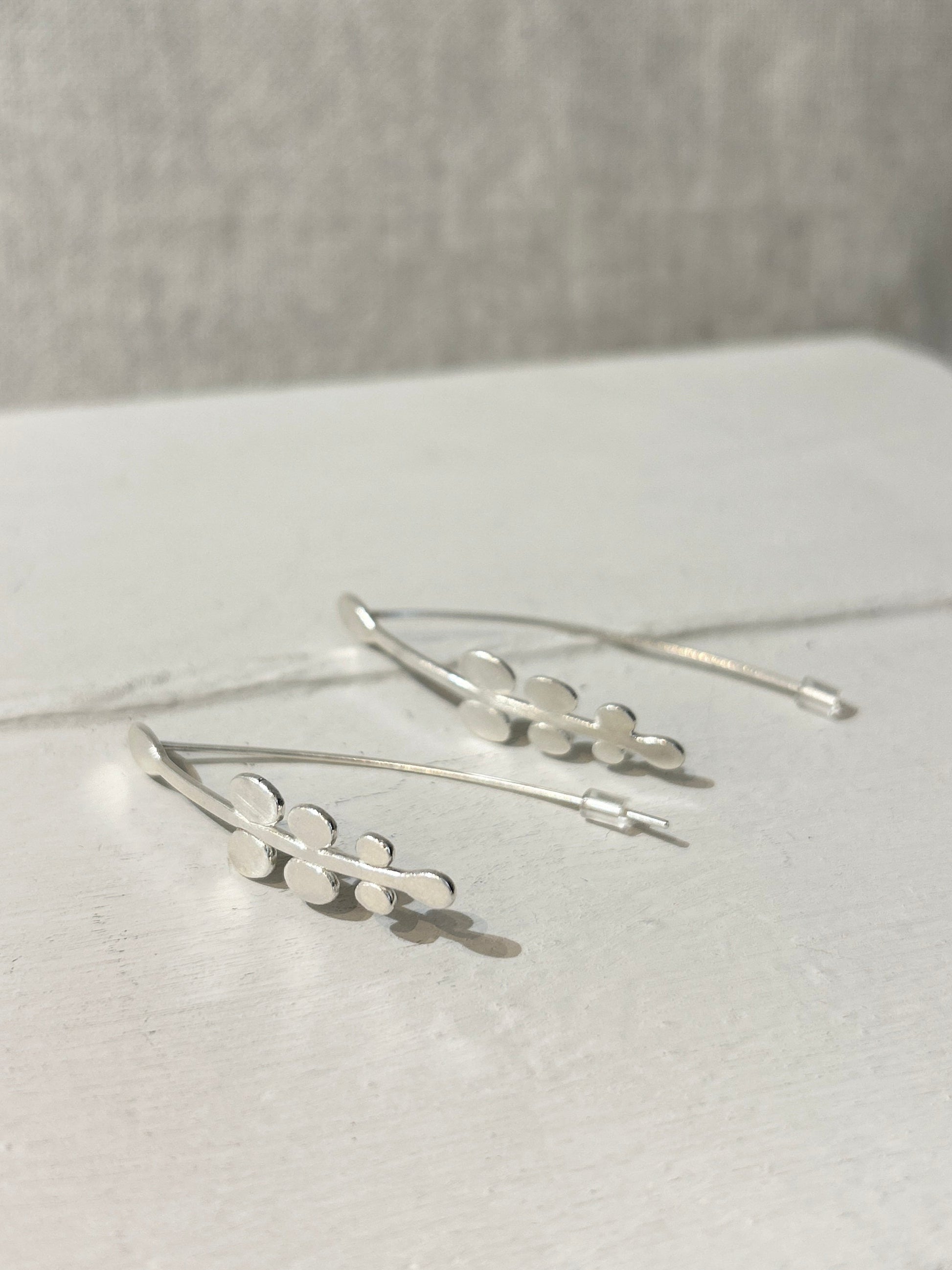 Silver earrings on a white surface with a neutral background