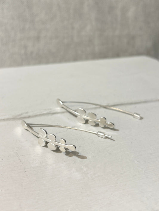 Silver earrings on a white surface with a neutral background
